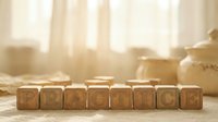 Wooden letter blocks spelling PRACTICE arranged on rustic table in warm sunlit kitchen setting for educational and motivational concepts.