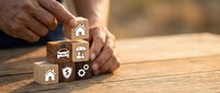 Hands arranging wooden blocks with insurance icons including home, car, health and financial protection symbols on rustic table for coverage planning.