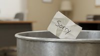 Crumpled note with the word Sorry thrown into a metal trash can in an office, symbolizing rejected apology or failed communication.