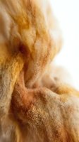 Soft golden wool fiber in warm amber and rust tones, macro close-up showing natural texture and fluffy layers for craft and textile backgrounds.