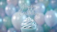 Cupcake with blue frosting and a silver Happy Birthday topper, surrounded by soft pastel balloons in a dreamy celebration setting.