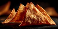 Golden crispy tortilla chips arranged in triangular stack on dark surface with warm lighting, ready for snacking, appetizers, and Mexican cuisine presentations.