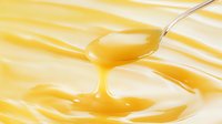 Dripping golden honey from silver spoon against blurred yellow background, macro close-up showing viscous texture and natural sweetness flowing in smooth motion.
