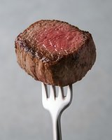 Juicy medium rare beef tenderloin steak piece on silver fork against gray background, showing perfect pink center and seared brown crust. Restaurant quality meat.
