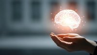 Glowing brain hologram floating above open palm representing artificial intelligence, innovation and mental health concepts in modern office setting.