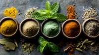 Aromatic spices and herbs in wooden bowls on dark stone background, colorful cooking ingredients with fresh mint leaves and bay leaves.