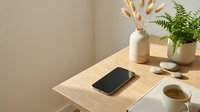 Minimalist wooden desk setup with smartphone, coffee cup, decorative vase and green plant creating peaceful workspace atmosphere for productivity and focus.