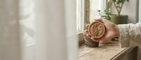 Person holding vintage compass with brass finish near window with natural light and potted plant, symbolizing direction and navigation for travel or business concepts.