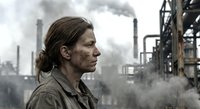 Determined female industrial worker in protective gear at oil refinery with smoking chimneys and heavy machinery in background for safety campaigns.