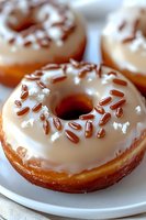 Fresh baked donuts with white vanilla glaze and chocolate sprinkles on white plate, extreme close up macro food photography with selective focus.