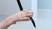 Senior adult hand with wrinkled skin gripping black rope or cord against neutral background, representing strength, determination, or resilience in aging population for healthcare and wellness content.