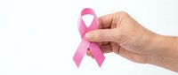 Hand holding pink ribbon symbol for breast cancer awareness campaign on white background. Support healthcare cause and medical research fundraising.