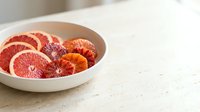 Sliced grapefruit and citrus fruits arranged in white bowl on marble countertop for food styling and culinary content.