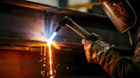 Professional welder in protective mask performing arc welding with bright sparks and flames in industrial workshop setting for manufacturing projects.