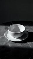 White ceramic bowl and saucer on dark marble surface with dramatic lighting, suitable for tableware, kitchenware, and minimalist design projects.