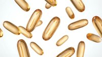Golden vitamin capsules scattered on white background for health and wellness supplement advertising and medical nutrition concepts.