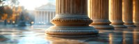 Classical marble columns with ornate bases in warm sunset light, reflecting on wet surface. Architectural detail of historic government or educational building entrance.