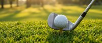 Golf club and ball on green grass course with warm sunlight creating golden hour atmosphere for sports and recreation activities.