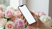 Hand holding smartphone with blank white screen against bouquet of pink and cream roses, suitable for app mockups, mobile marketing, floral design promotions, and digital product displays.