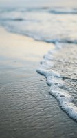 Soft ocean waves gently rolling onto sandy shore with shallow water and foam creating a serene coastal scene, suitable for travel, wellness, and nature-themed designs.