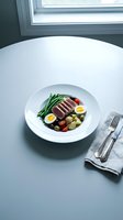 Sliced seared tuna steak served with green beans, boiled eggs, potatoes, and tomatoes on white plate in fine dining restaurant setting.
