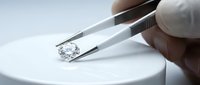Jeweler or gemologist examining a diamond with tweezers and loupe on white surface, close-up of professional gemstone evaluation and quality assessment.