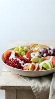 Fresh fruit platter with grapes, apples, pomegranate seeds and citrus arranged on white ceramic plate for healthy eating and entertaining.