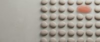 White pharmaceutical pills arranged in organized rows with one distinctive pink tablet standing out among uniform medication on neutral background.