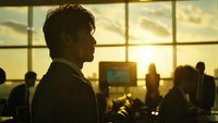 Professional businessman silhouette in modern office during golden hour sunset with colleagues working in background for corporate presentations.