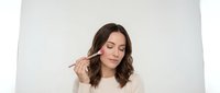 Young brunette woman applying makeup with brush against clean white background for beauty and cosmetics advertising campaigns.