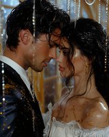 Romantic couple in elegant formal wear sharing intimate moment under sparkling lights at luxury celebration event with golden bokeh background.