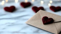Romantic composition with burgundy glitter heart on craft paper envelope against blurred hearts and bokeh lights background, love message concept.