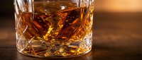 Golden whiskey in crystal cut glass tumbler on wooden surface with warm ambient lighting for luxury beverage advertising and bar concepts.