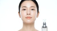 Young Asian woman with clear glowing skin holding cosmetic serum bottle for skincare routine and anti-aging treatment on white background.