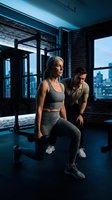 Fit senior Caucasian woman doing dumbbell lunges with male personal trainer in modern gym at dusk, active aging and healthy lifestyle concept.