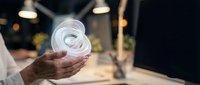 Close-up of hands holding glowing spiral light bulb in modern office environment, symbolizing innovation, creativity, and sustainable energy solutions for business concepts.