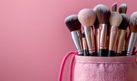 Professional makeup brushes set in pink glitter cosmetic bag against rosy background. Essential beauty tools for applying foundation, powder, blush and eyeshadow.