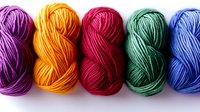 Colorful yarn skeins arranged in row showing vibrant purple, orange, red, green and blue wool threads on white background, ready for knitting and craft projects.