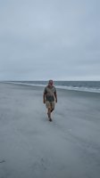 Middle-aged Caucasian male jogging along empty sandy beach under overcast sky, wearing casual athletic wear, ideal for wellness and outdoor fitness concepts.