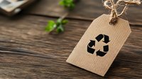 Recycling symbol on kraft paper tag with twine string against rustic wooden background with green plant leaves, eco-friendly concept for sustainable living.