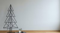 Geometric wire frame Christmas tree sculpture on wooden surface with minimalist white wall background and small potted succulent plant.