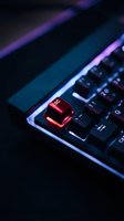 Gaming keyboard with glowing red escape key in dark cyberpunk lighting for technology and computer hardware concepts.