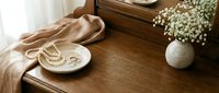 Elegant wooden dresser with pearl jewelry, silk scarf and white flowers in ceramic vase creating luxurious bedroom interior styling for home decor.