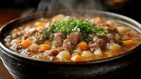 Hot steaming beef stew with tender meat chunks, carrots, potatoes and fresh herbs in rustic ceramic bowl, served homestyle with rich brown gravy.