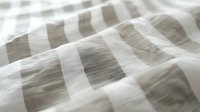 Soft white and gray striped bedding fabric with gentle folds and wrinkles creates cozy, minimalist texture for modern bedroom interior design and textile backgrounds.