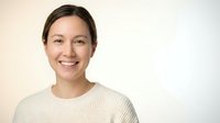 Happy Asian woman in beige sweater smiling warmly at camera against neutral background for lifestyle and wellness content.