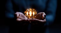 Glowing magical sphere with burning candles floating between cupped hands in dark atmospheric setting, creating mystical illumination and bokeh effect.