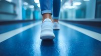 White sneaker on person walking along blue corridor with modern lighting, low angle view focused on footwear against blurred background perspective.