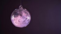 Transparent glass bauble filled with swirling pink and purple smoke or fog effect, suspended against dark background for holiday decoration and festive design projects.