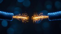 Dramatic electrical spark between two copper wires with bright orange sparks and blue glow against dark background with bokeh effect. For technology concepts.